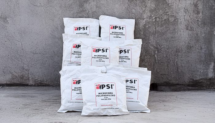 Un grupo de bolsas de Microfibra de Polipropileno PSI apiladas en forma de pirámide sobre una superficie de concreto, con una pared gris de fondo.