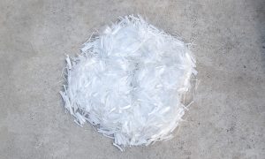 Microfibras de polipropileno PSI blancas de 19 mm esparcidas sobre una superficie de concreto, mostrando su textura ligera y uniforme para refuerzo de concreto.